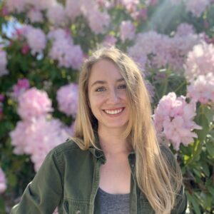 Headshot of MCB PhD student Samantha (Sam) Rider, standing in front of pink flowers